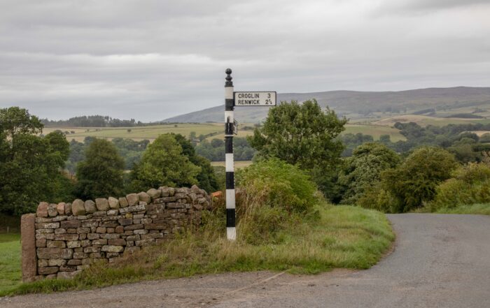 Image of old black and white fingerpost sign with hills behind