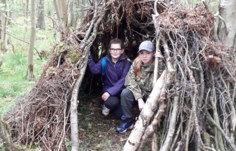 Image of two children sitting inside a shelter made from tree branches