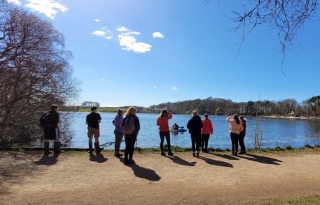 Image of group standing by a lake in sunshine with a blue sky