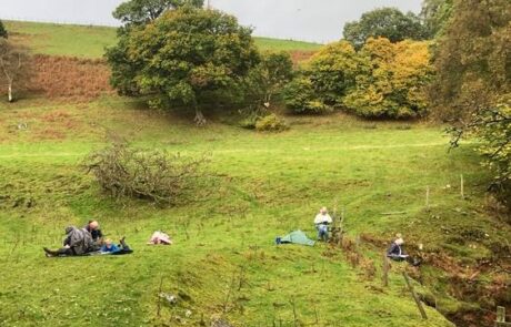 Photo of people in a field by a river sketching