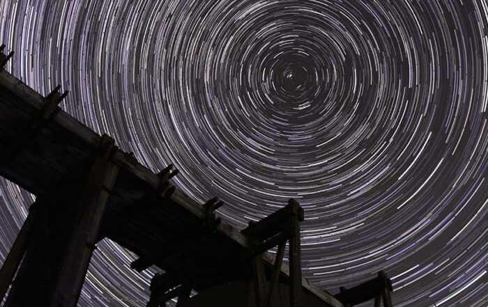 Image of star trails against dark sky with silhouette of mine machinery