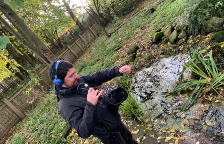 Image of man standing by a pond holding out a microphone to record sound