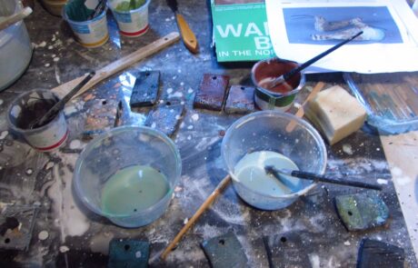 Photogrpah of ceramic glazes in pots on a table with brushes