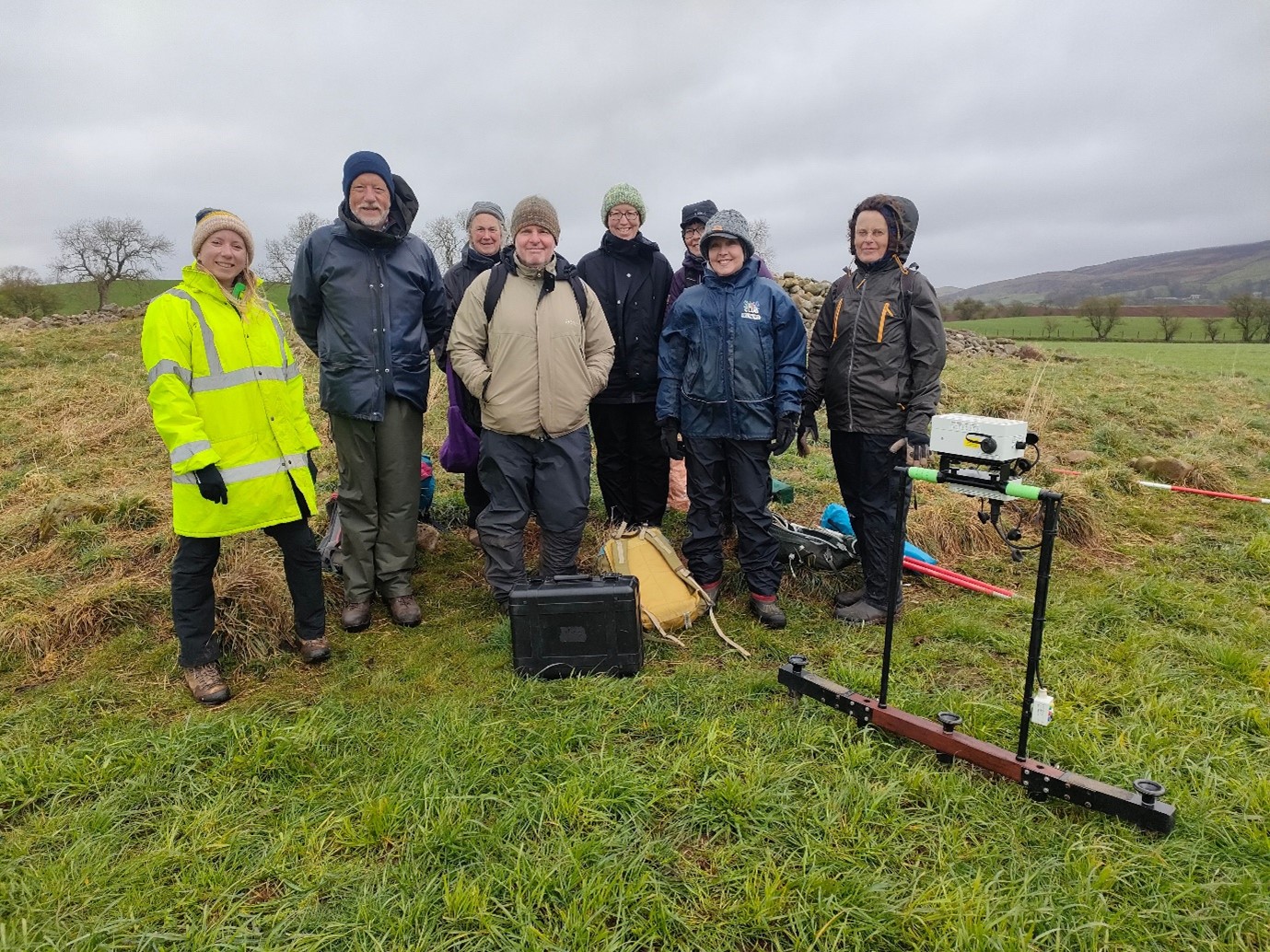 Photo of group of people in a field with archaeological survey equipment