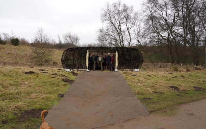 Image of round house structure made of natural materials with people standing in the entrance