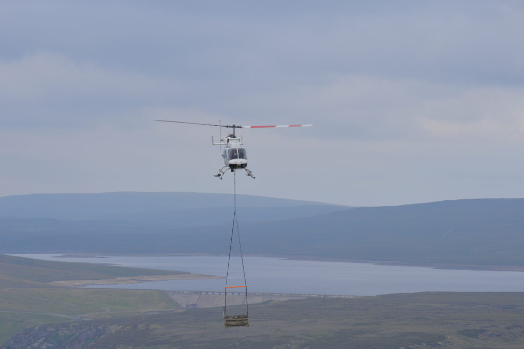 Helicopter airlifting a stone dam by Cow Green Reservoir
