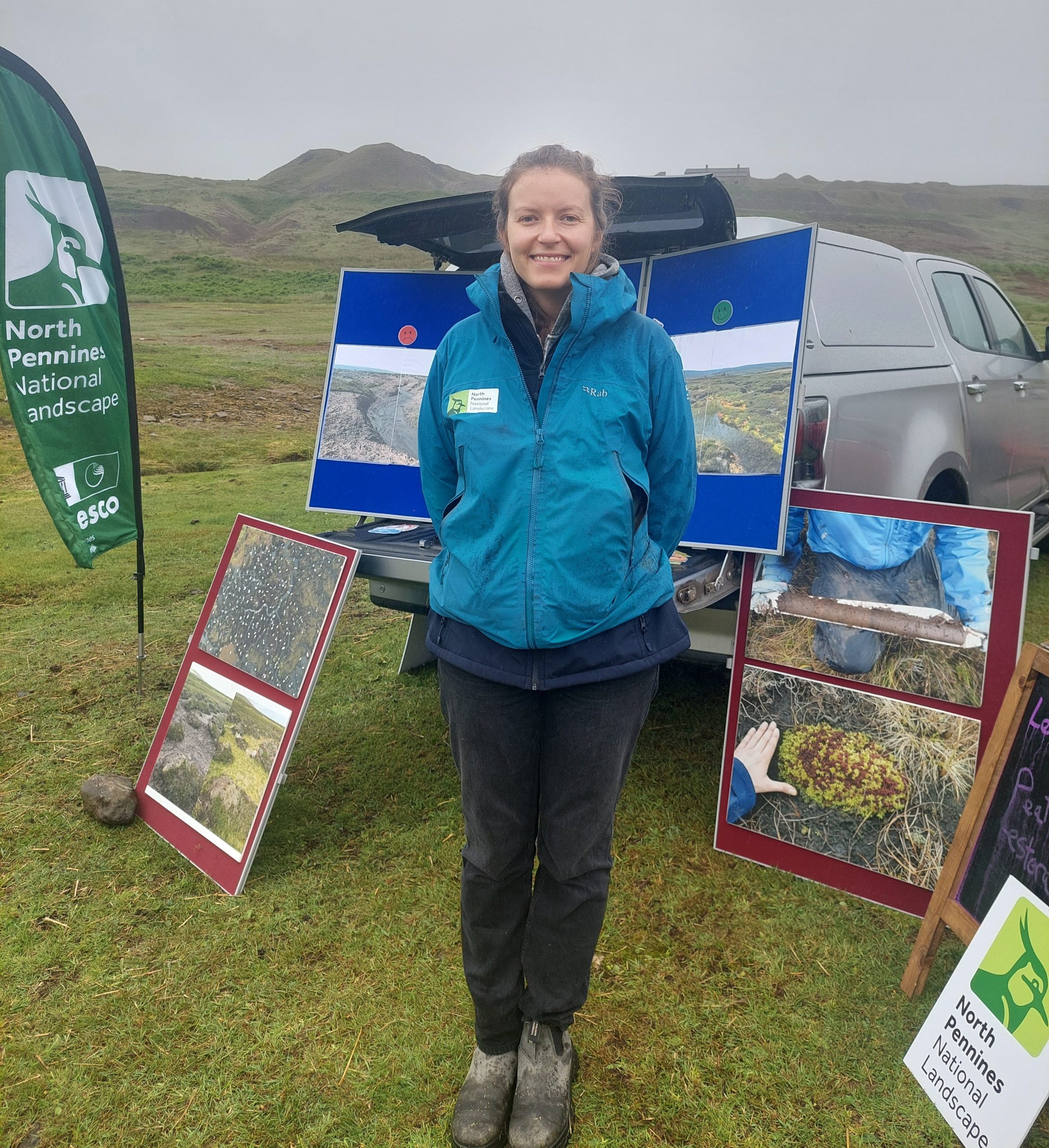 North Pennines field officer smiling and standing in front of North Pennines National Landscape team's outdoor stand, at the Let's Learn Moor event.