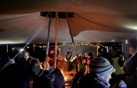 11_Stars and stories_281024_NPNL & Shane Harris Adults dressed in winter clothes and sitting under large tent at stars and stories stargazing event. Fire in the centre.