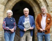 Pendlebury Award winners standing with the smiling director of the North Pennines National Landscape in front of a stone arched entranceway. The person in the middle is holding the award.