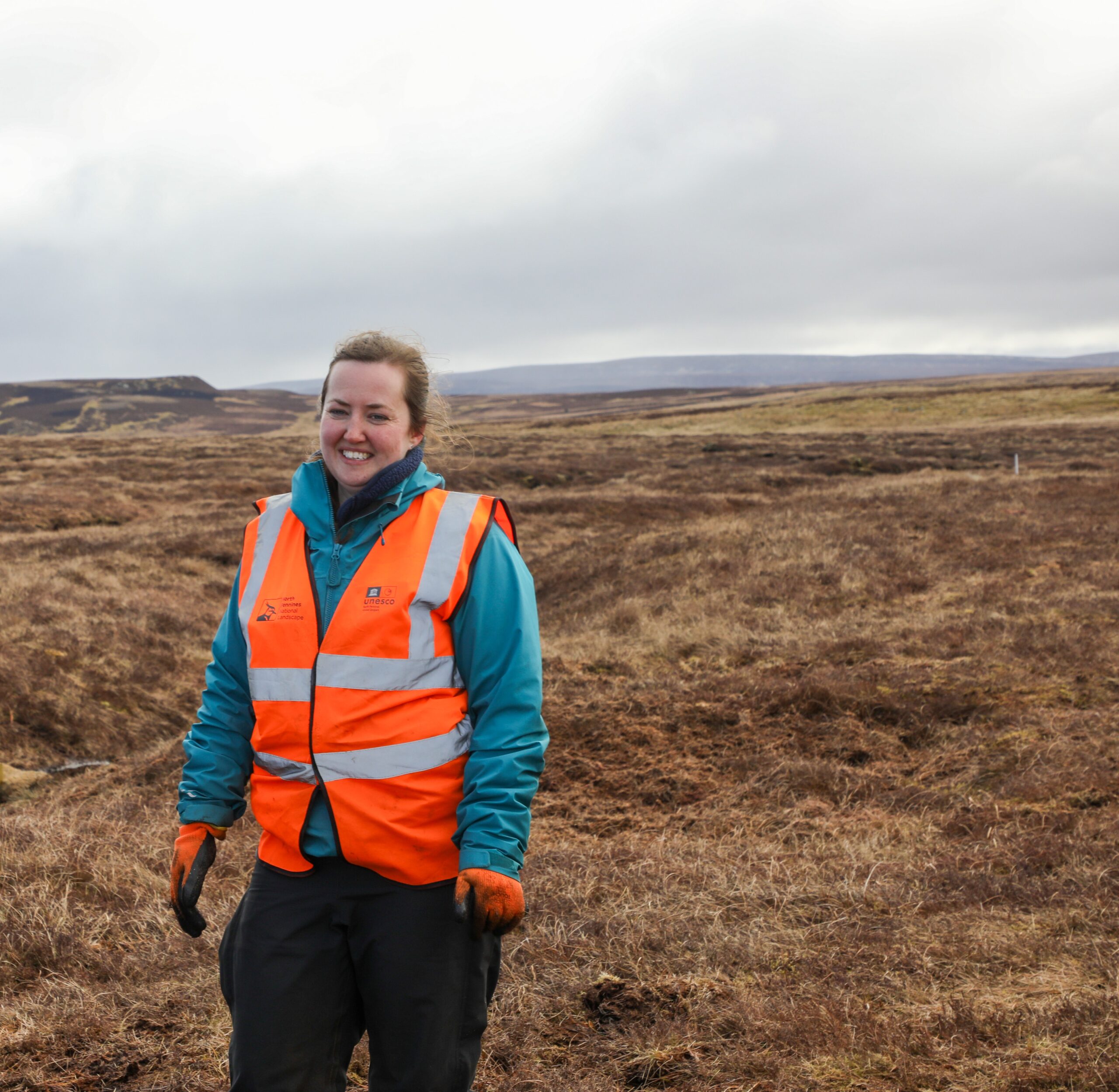 Senior peatland field officer in high-vis jacket smiling and standing on a North Pennines peatland.