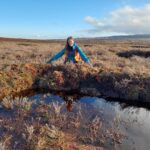 Senior peatland field officer Lisa Gill crouching next to scallop bund, Scargill, December 2025