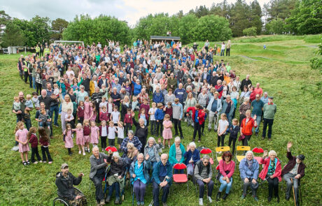 Members of Alston Moor Community raise their hadn to show they were at the last Community Photo taken in 1999. Fairhills Recreation Ground, 2026 Alston community mass photo Group of people sitting and standing in a field for the Alston Moor community mass photo 2026